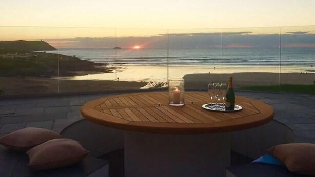 A round wooden table with a bottle and glasses, overlooking a beach at sunset. - The White House (Wadebridge)