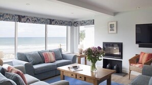 A modern living room with a large window overlooking the ocean, a flat-screen TV, and a fireplace. - The White House (Wadebridge)