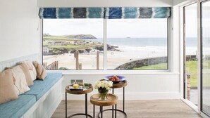 A room with a view of the beach, a blue sofa, and two small tables with drinks and flowers. - The White House (Wadebridge)