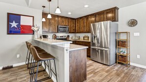 Une cuisine dotée de meubles en bois, d’appareils électroménagers en acier inoxydable, d’un coin bar et d’une décoration à l’effigie du drapeau du Texas.