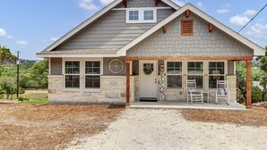 Une maison à deux étages avec une façade en pierre, un porche couvert avec des chaises et une pancarte de bienvenue.