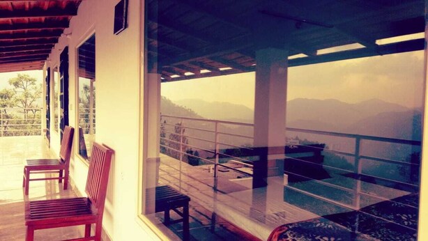 A balcony with a view of a mountainous landscape, wooden benches, and a glass railing.
