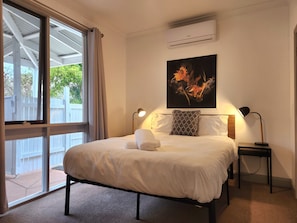 A hotel room with a bed, two bedside lamps, a wall-mounted air conditioner, and a window with curtains.