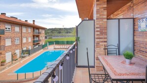 A balcony with a view of a swimming pool, a table with a potted plant, and a brick building in the background.