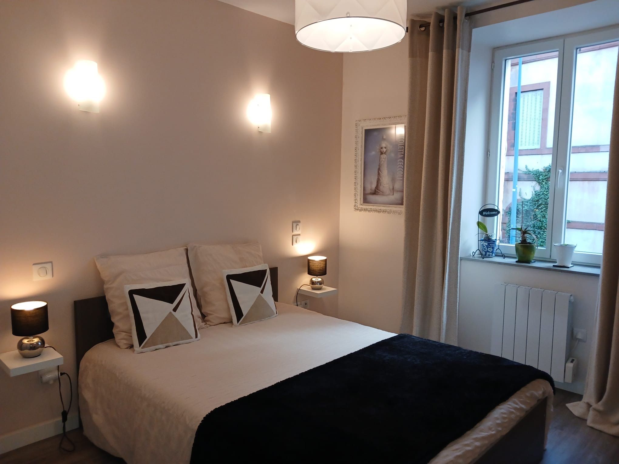 Une chambre à coucher avec un lit, des lampes de chevet, une fenêtre avec des rideaux et un radiateur.