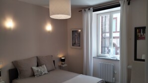 A bedroom with a bed, bedside lamps, a window with curtains, and a radiator. - La Dolce Vitae (Rodez)