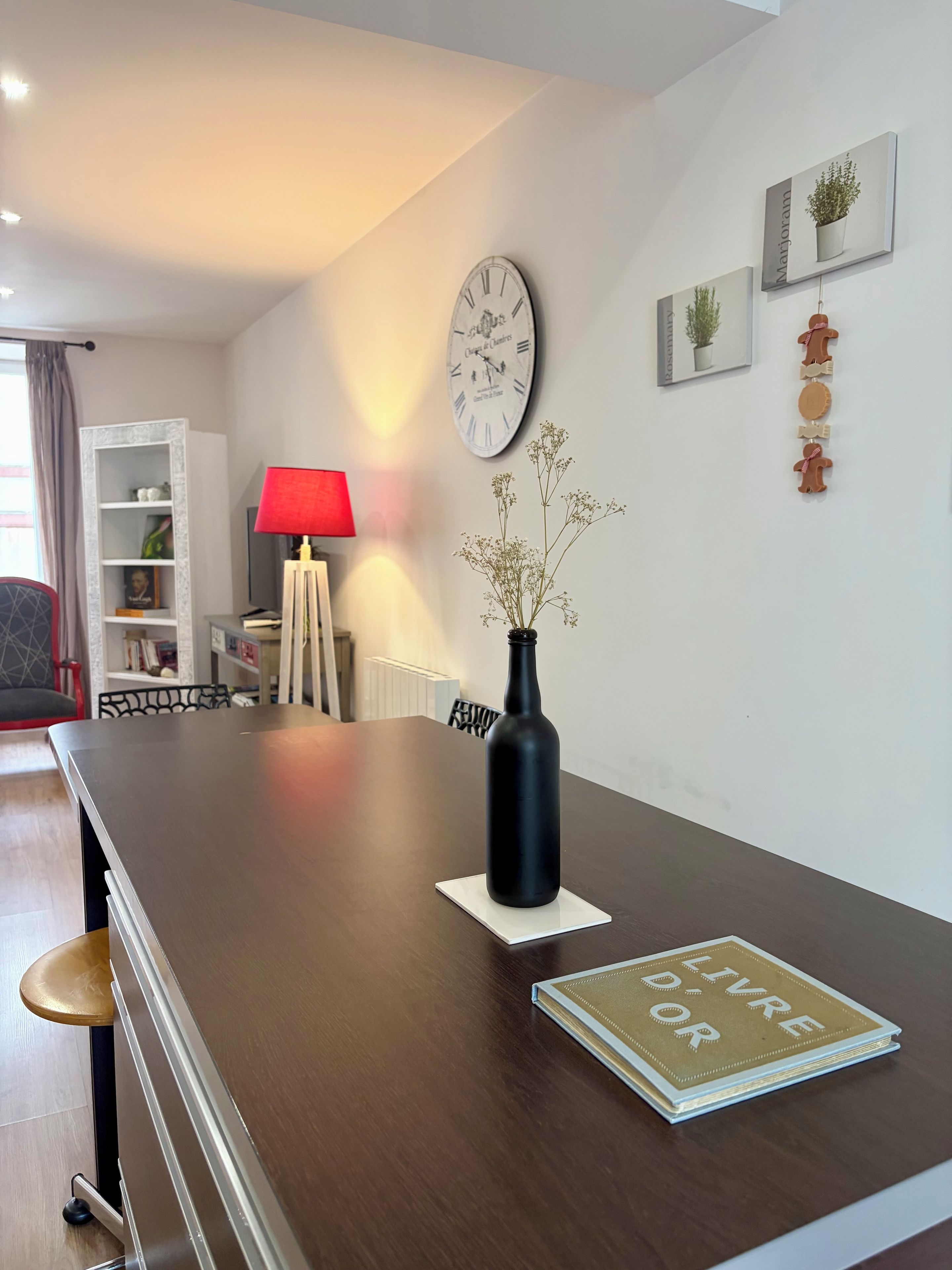 Ein modernes Wohnzimmer mit einem Holzesstisch, einer schwarzen Vase mit Blumen, einer roten Lampe und einer Wanduhr.