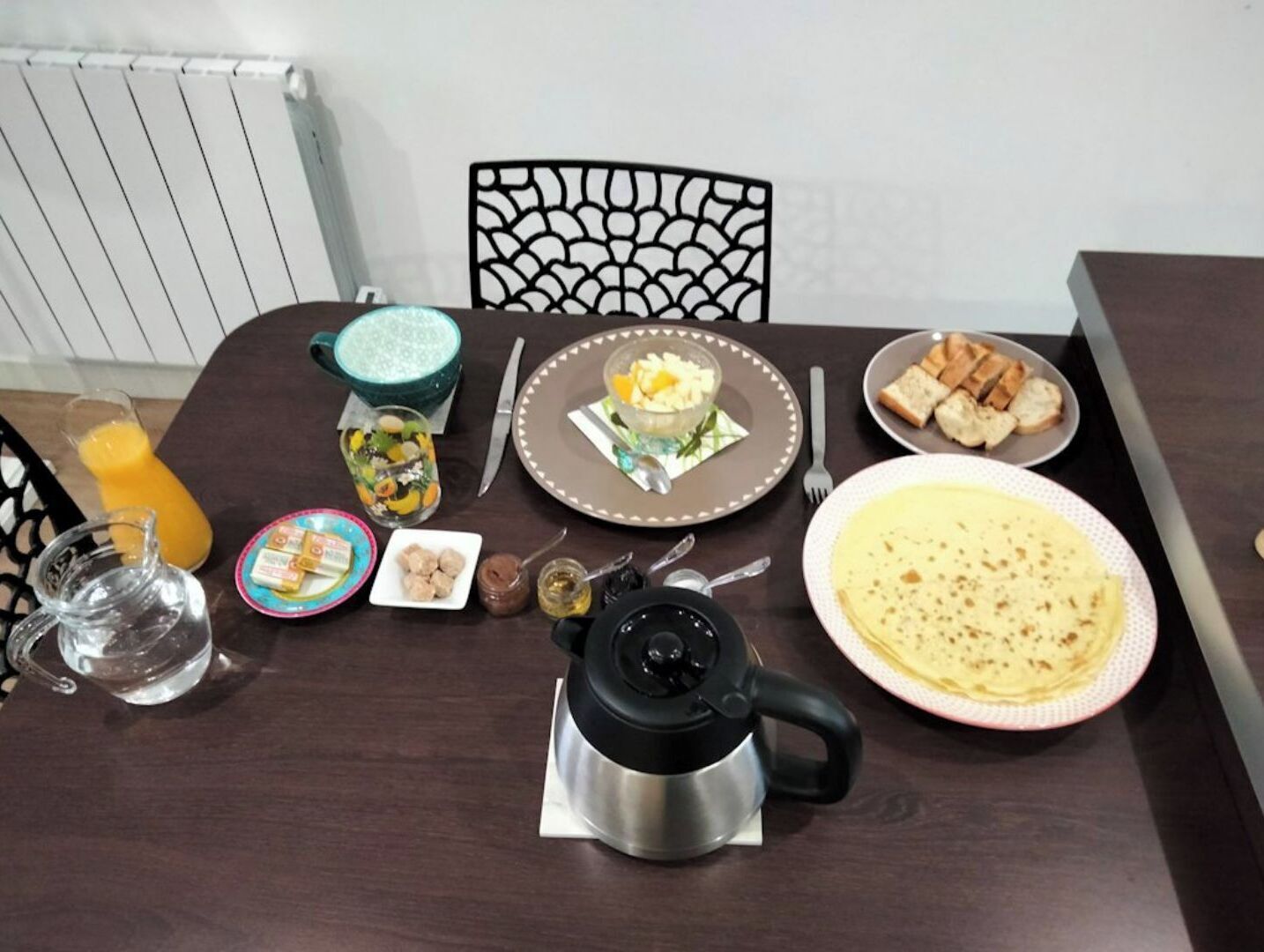 Une table à manger avec divers aliments pour le petit-déjeuner, notamment des tartines, un bol de fruits, une tasse de café et un pichet de jus d’orange.
