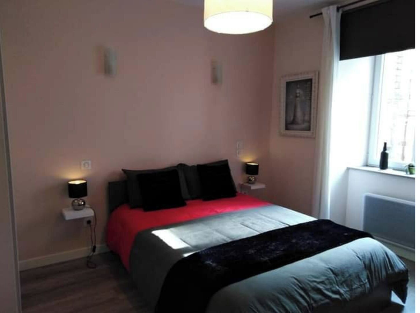 A bedroom with a bed, two bedside lamps, a window with a view, and a radiator.