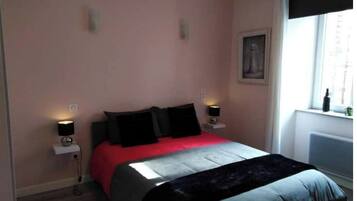 A bedroom with a bed, two bedside lamps, a window with a view, and a radiator.
