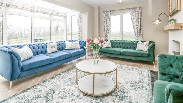 A spacious living room with a blue sectional sofa, a green sofa, and a round coffee table. - Orchard House (Leominster)