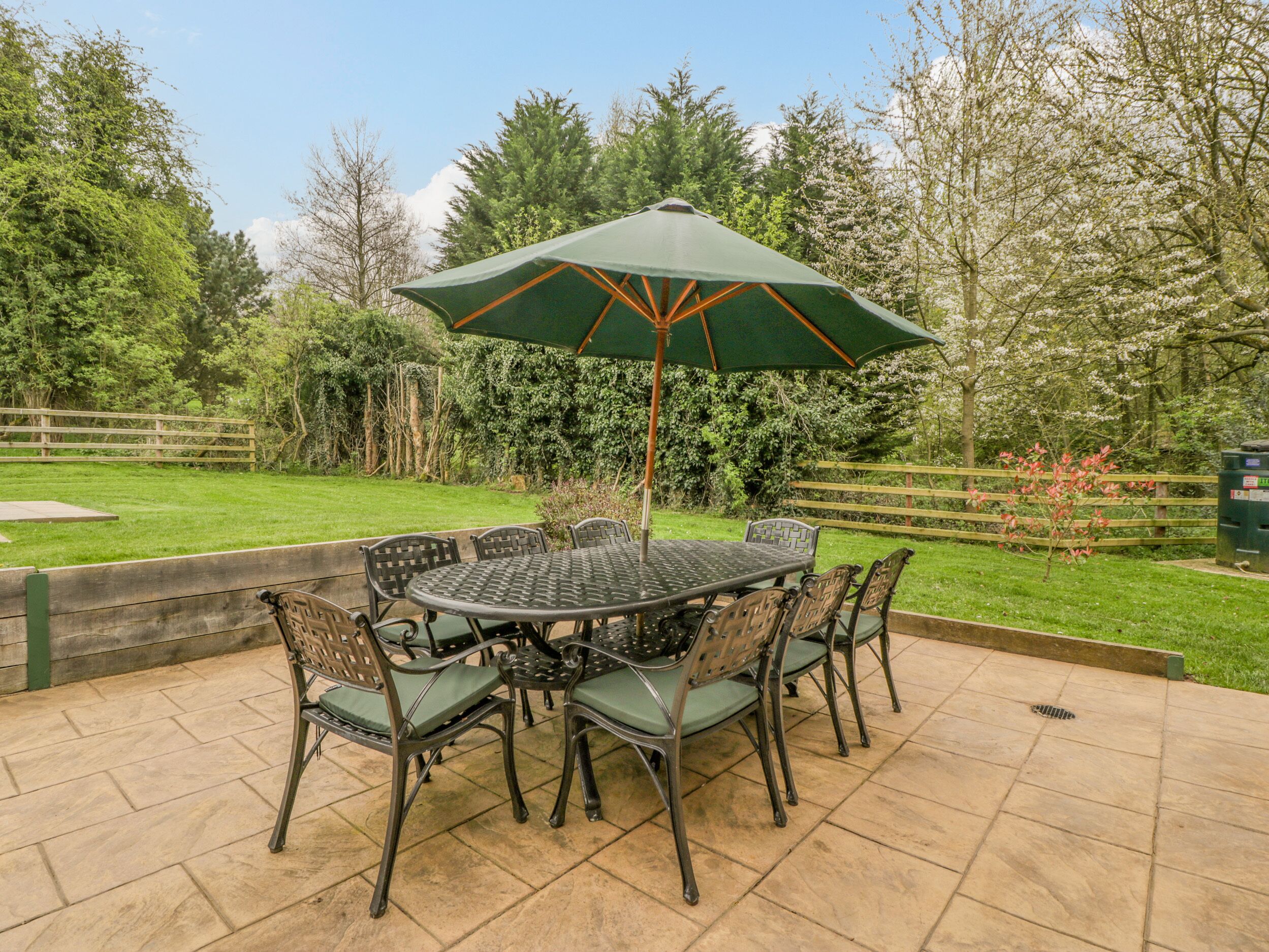 A patio with a round table and chairs, an umbrella, and a wooden fence in the background.