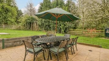 A patio with a round table and chairs, an umbrella, and a wooden fence in the background.