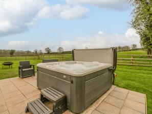 A hot tub with a cover, two chairs, and a small table on a patio with a grassy field in the background.
