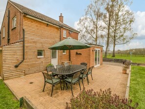 A patio with a table and chairs, a brick house, and a lawn.