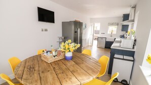 A dining area with a wooden table and yellow chairs, a kitchen in the background, and a flat-screen TV mounted on the wall. - Orchard House (Leominster)