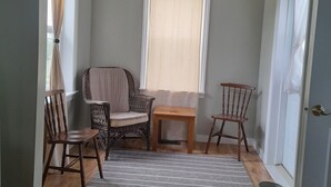 Ein Zimmer mit Holzboden, einem Korbstuhl, einem kleinen Holztisch und einem Fenster mit transparenten Vorhängen.