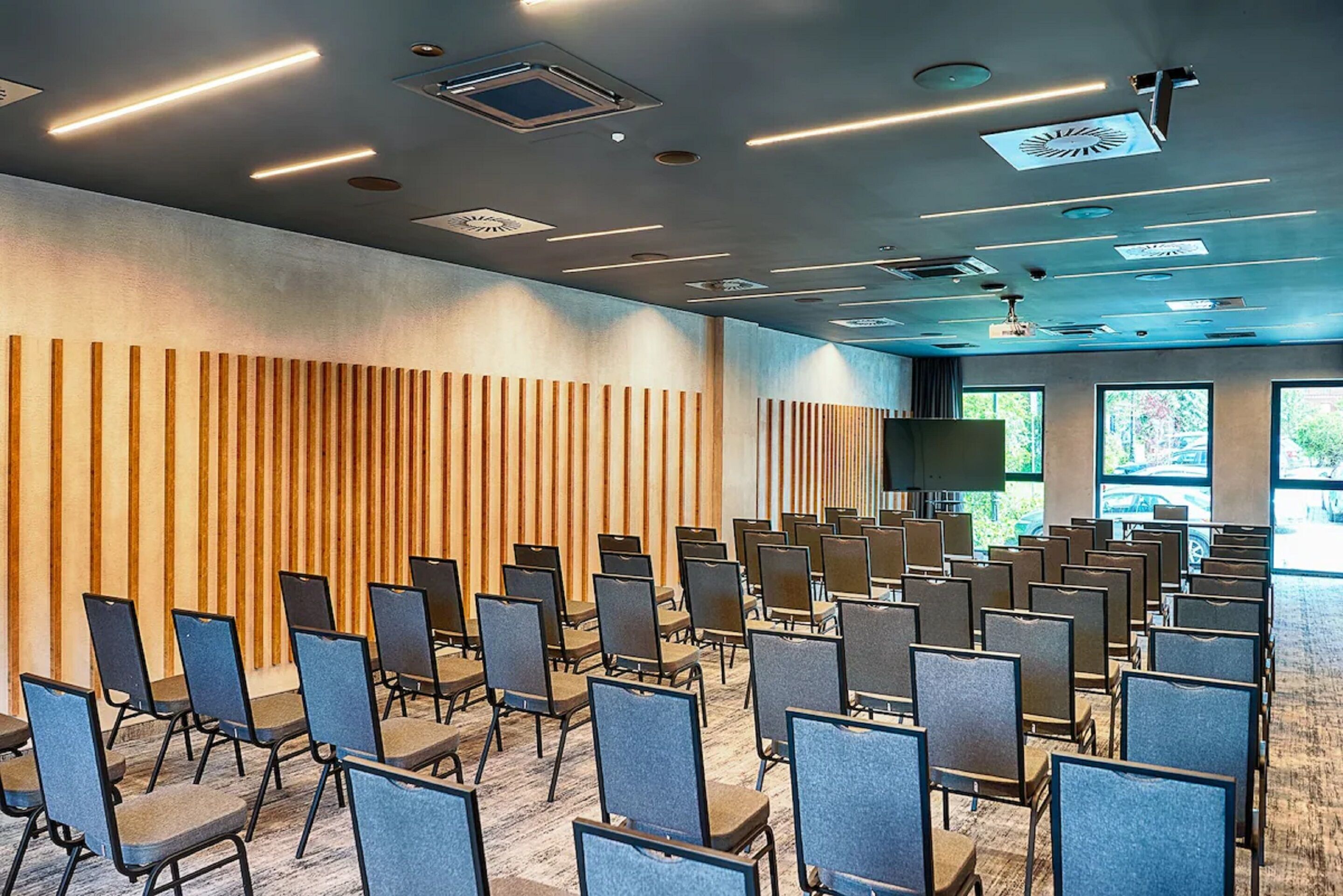 A conference room with rows of chairs, a wooden panel wall, and ceiling lights.