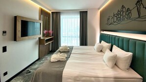 Habitació d'hotel amb un llit, una televisió, una obra d'art penjada a la paret i una finestra amb cortines.
