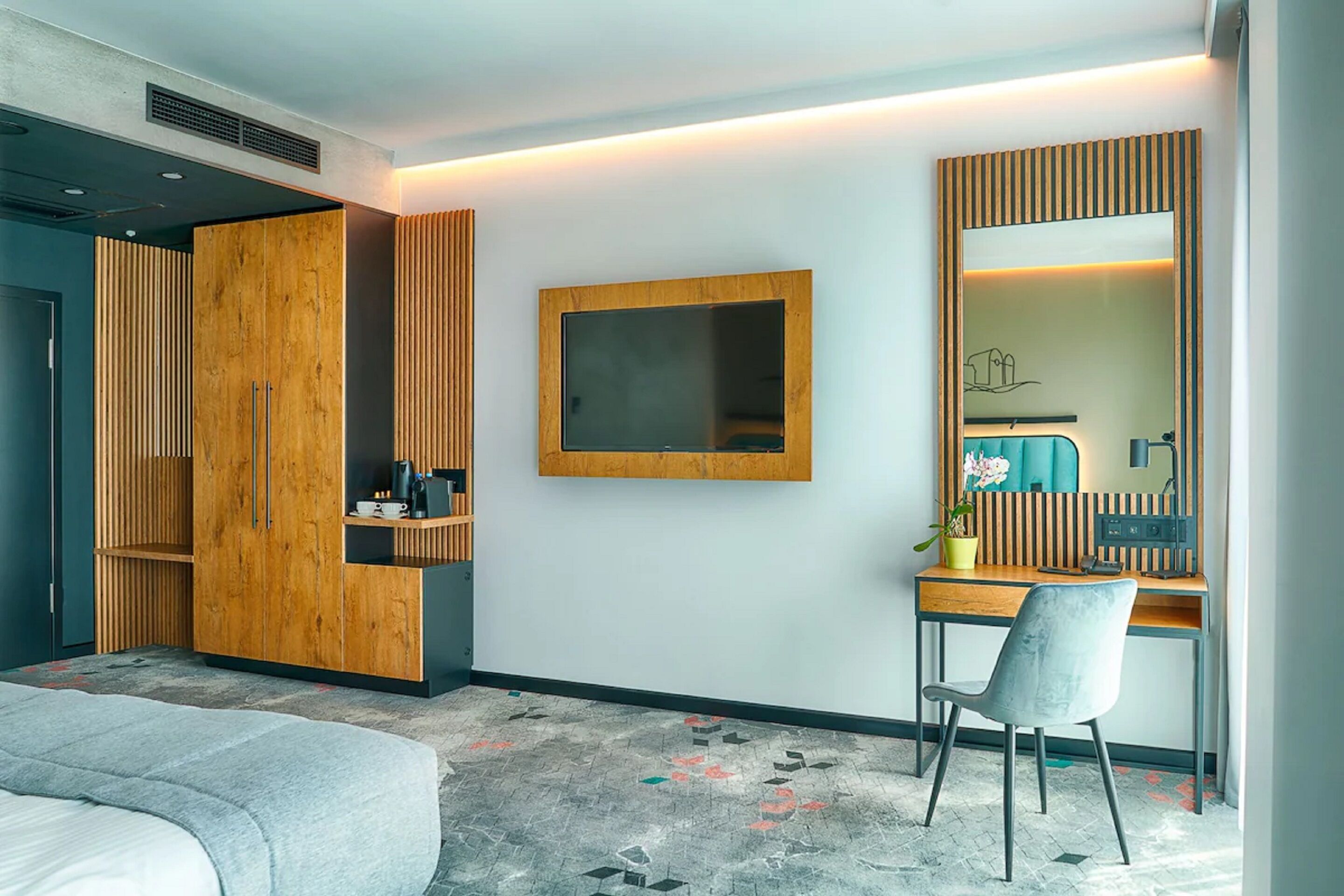 Una habitación de hotel moderna con una cama, un escritorio con silla, un espejo grande y un armario.