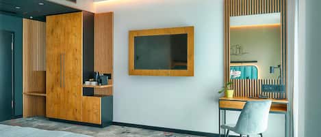 A modern hotel room with a bed, a desk with a chair, a large mirror, and a wardrobe.