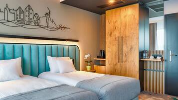 A modern hotel room with two beds, a cityscape mural, a wooden wardrobe, and a small side table with a plant.