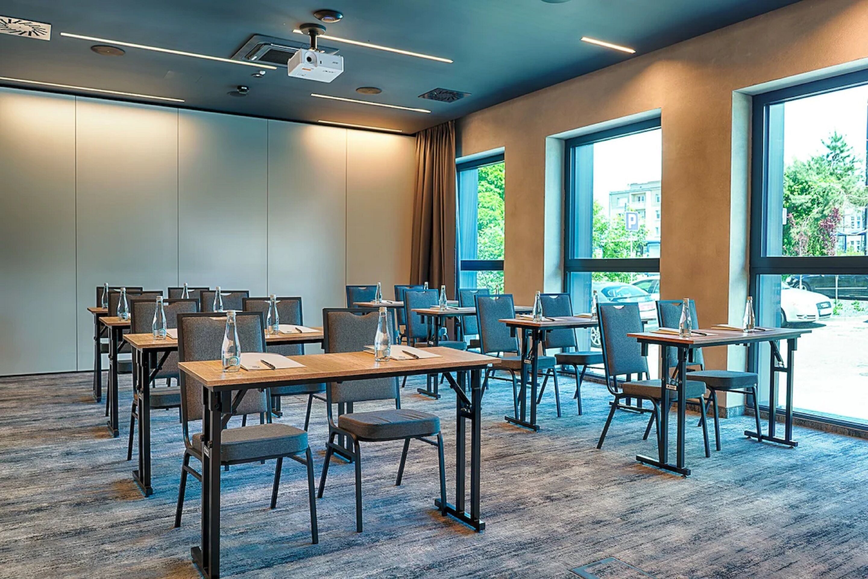A conference room with tables and chairs, large windows, and a projector on the ceiling.