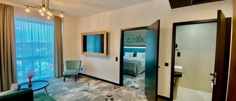 A hotel room with a bed, a chair, a small table, and a view of the city.