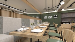 Un restaurant modern amb taules de fusta llargues, caires tapissades de verd i una zona de cuina al fons.