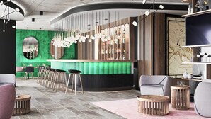 Zona de bar moderna amb una paret d'accent verd, mostrador de bar de fusta i diverses opcions de seients, incloent tamborets d'alta i taules rodones.