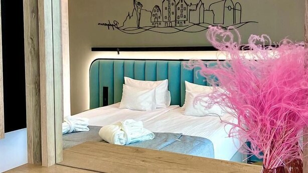 A neatly made bed with white linens, a teal headboard, and a wall mural depicting a town scene. - Focus Hotel Premium Bydgoszcz (Bydgoszcz)