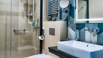 Un baño moderno con cabina de ducha de vidrio, inodoro blanco, lavabo grande con espejo y toallero.