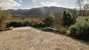 A gravel area with a stone wall and a view of a forested hillside. - The Old Smithy Cottage (Blaenau Ffestiniog)
