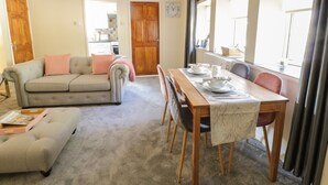 A cozy living room with a sofa, ottoman, and a dining table set for two. - The Old Smithy Cottage (Blaenau Ffestiniog)