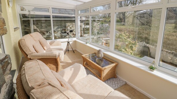 A sunroom with a large window, wicker furniture, and a telescope. - The Old Smithy Cottage (Blaenau Ffestiniog)