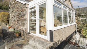 A stone house with a conservatory featuring large windows and a white exterior. - The Old Smithy Cottage (Blaenau Ffestiniog)