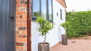 A brick building with a white exterior, a black door, and a window. There are two potted plants in front of the building. - Little Oakleigh (Llanymynech)
