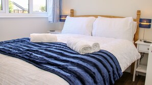 A neatly made bed with a blue and white duvet, a wooden headboard, and a bedside table with a lamp. - Little Oakleigh (Llanymynech)