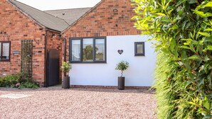 A brick house with a white exterior, a black door, and a small garden area with gravel and potted plants. - Little Oakleigh (Llanymynech)