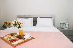A neatly made bed with white linens, a bedside table with a clock, and a tray with breakfast items including toast, eggs, and a glass of orange juice. - Art Hotel Batumi (Batumi)