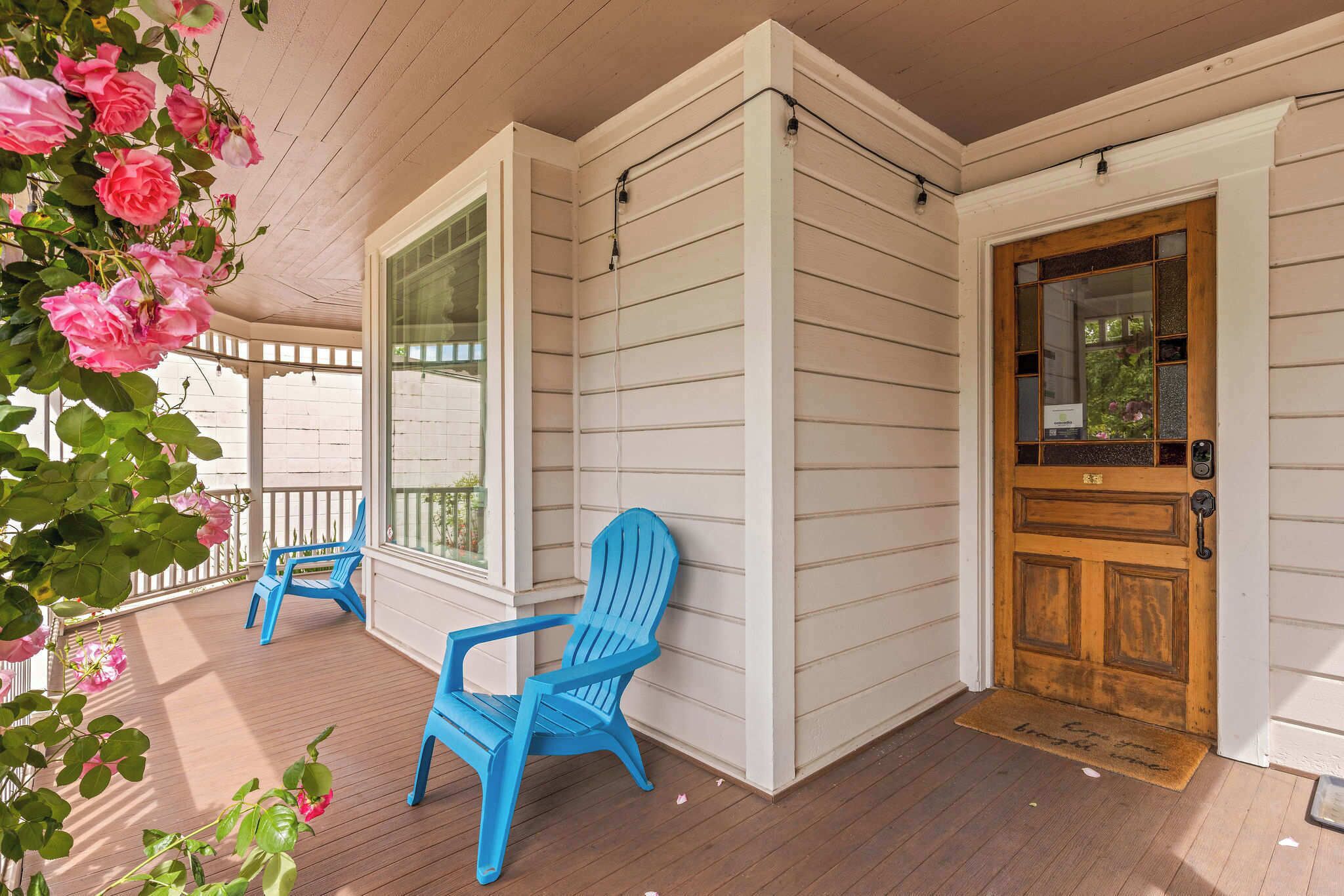 A porch with two blue Adirondack chairs, a wooden door, and a window.