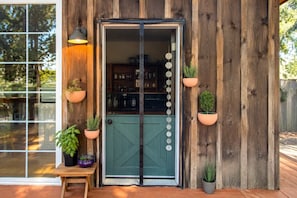 A wooden exterior with a glass door, potted plants, and a bench.