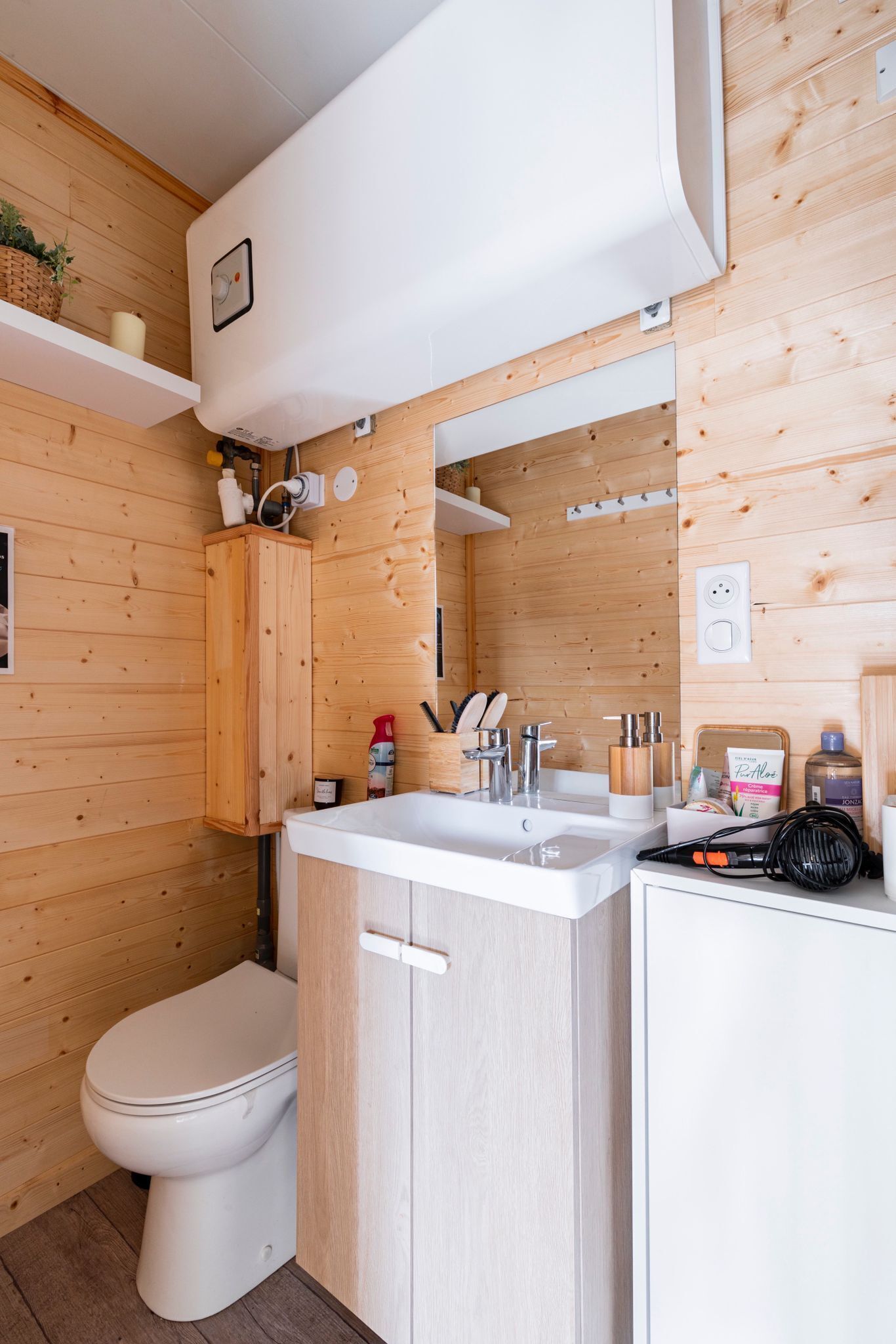 Een compacte, moderne badkamer met een wit toilet, houten kastjes, een wastafel met spiegel en een douchehoek.