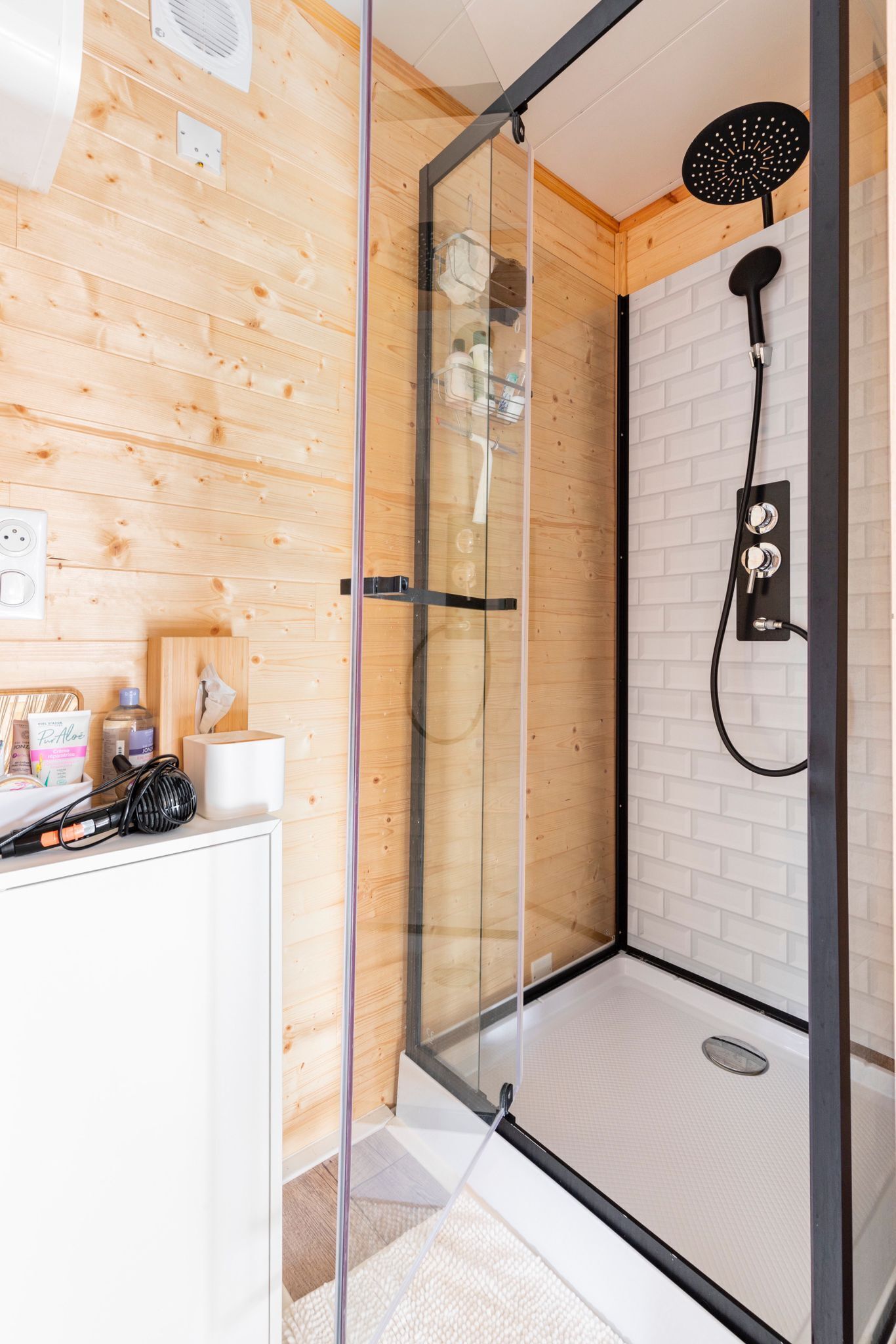 Une douche moderne avec un pare-douche en verre, un mur en bois et un sol carrelé de couleur blanche.