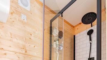 Une douche moderne avec un pare-douche en verre, un mur en bois et un sol carrelé de couleur blanche.