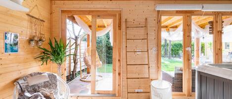 A wooden cabin interior with a cozy seating area, a hot tub, and a view of the outdoors.