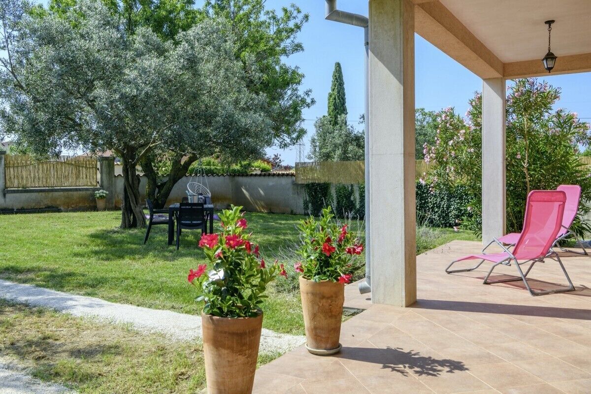 Ein überdachter Patio-Bereich mit zwei großen Kübelpflanzen, einem Grill und einem pinken Liegestuhl.