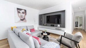 A modern living room with a grey sofa, a black coffee table, and a large flat-screen TV mounted on a white wall. - Charming Villa Audrey with an outdoor pool (Umag)