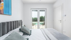 A bedroom with a bed, a nightstand, a lamp, and a view of an outdoor pool area through a sliding glass door. - Charming Villa Audrey with an outdoor pool (Umag)