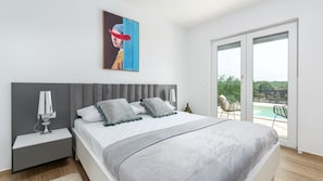 Quarto com cama, mesas de cabeceira, um quadro e vista para uma piscina através de uma porta de correr de vidro.